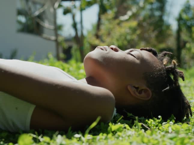 A young boy is lying on the grass and sleeping under a sunny sky