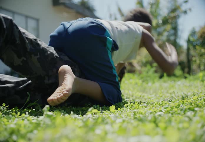 Brothers roughhousing over the green grass in the backyard at morning