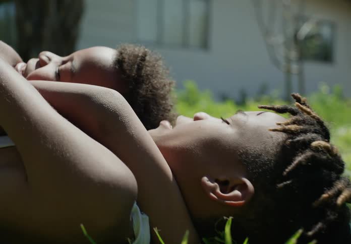 A big brother holding his little brother while they lie in the grass on a sunny day