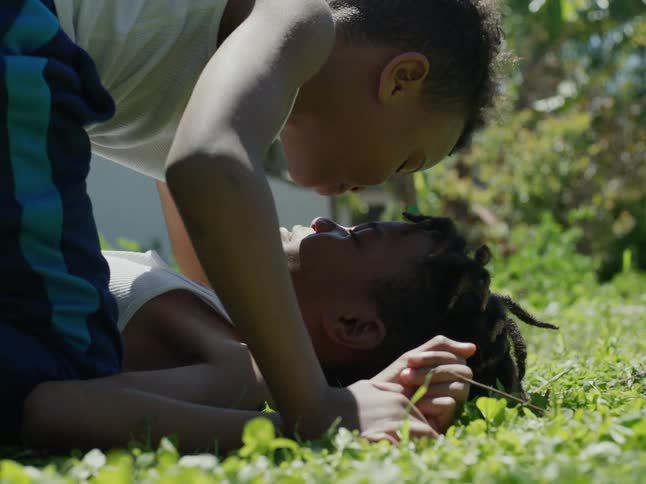 Tween brothers play wrestling in the grass in the summer in the back yard