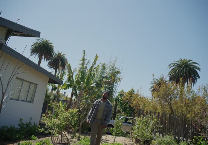 A man getting out of a car then walking through a yard and up to someone