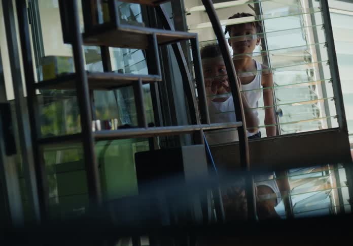Two young boys approach an open window and curiously peek inside