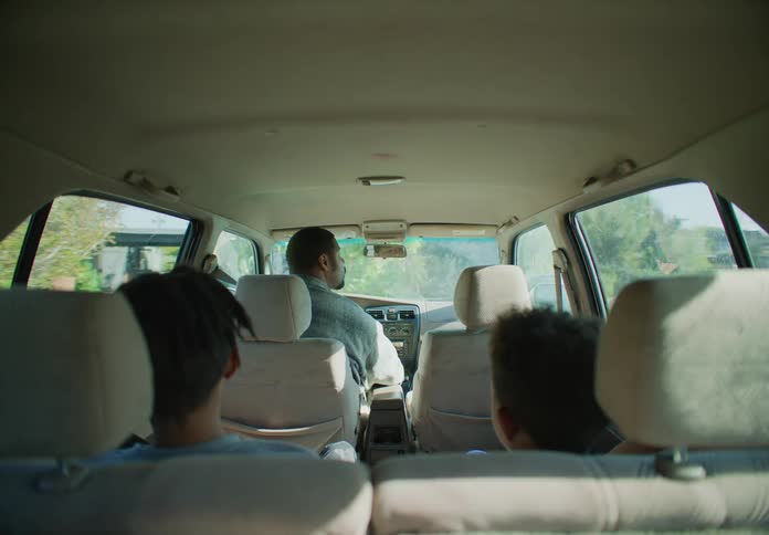 A father drives a vehicle while his two sons sit in the back seat togther