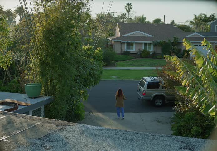 A woman walks to the end of her driveway as an suv is parked nearby