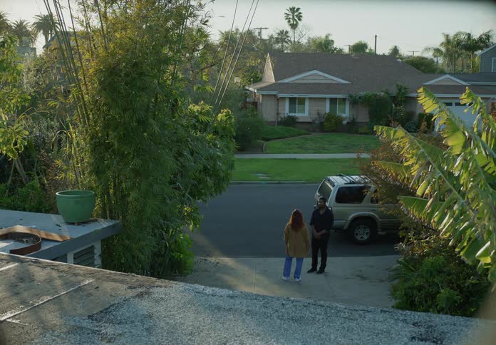 Two people are standing outside on a neighborhood sidewalk and talking