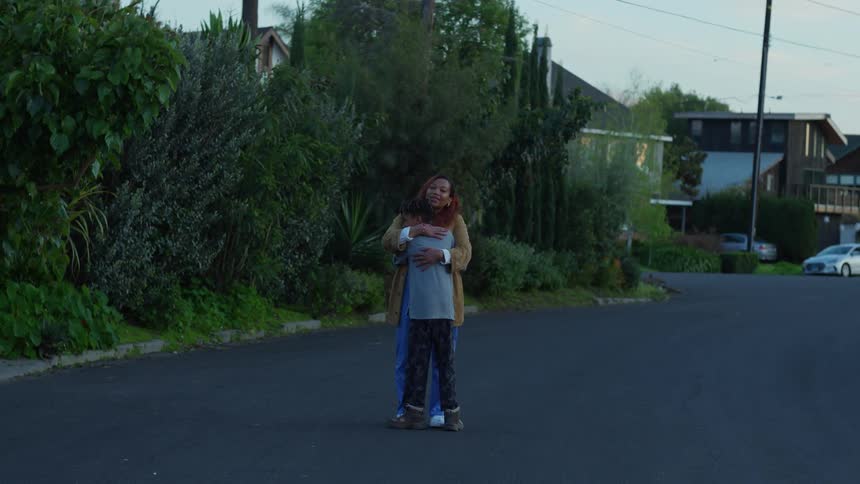 A woman hugs a boy while they stand on a neighborhood street during the day