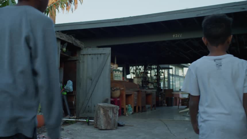 Two boys walk on a driveway and into a carport of a house at sunset