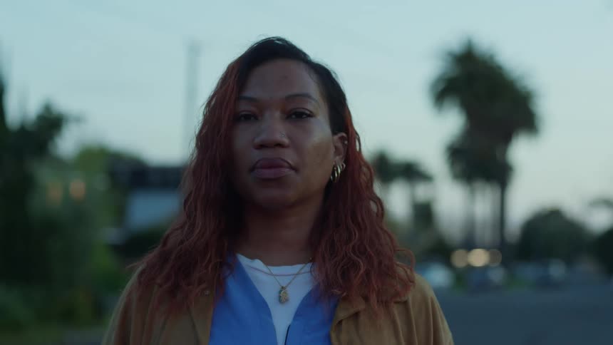 Woman with red curly hair earrings and necklace stares at camera in the street at dusk
