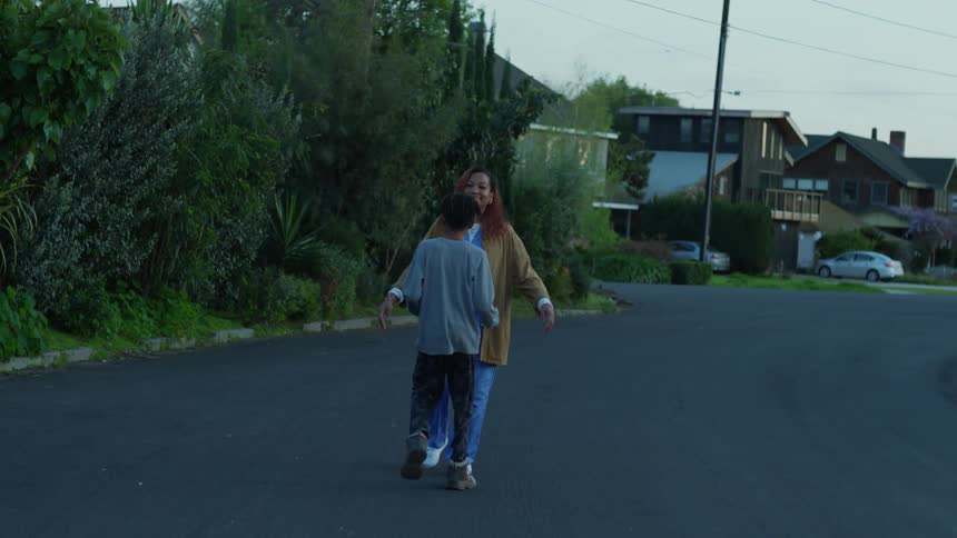Mother and son meeting on the neighborhood street hug each other at evening