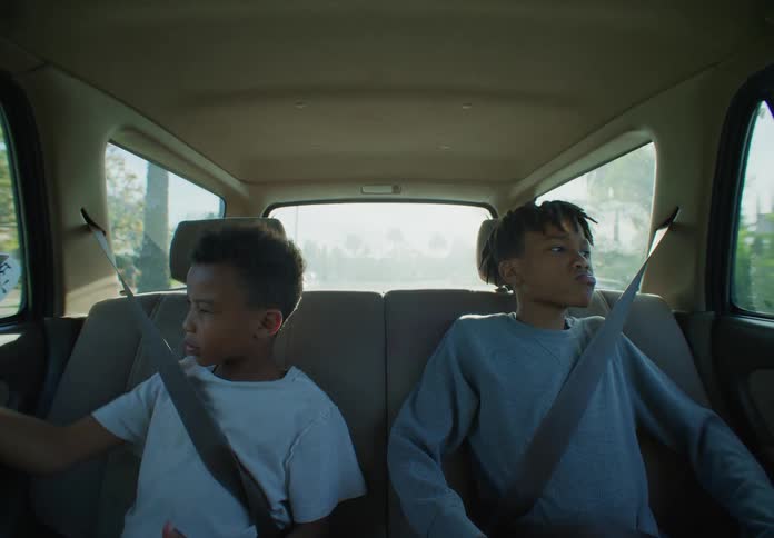 Two boys are sitting in the back seat of a traveling automobile with their seat belts on as they look out the windows