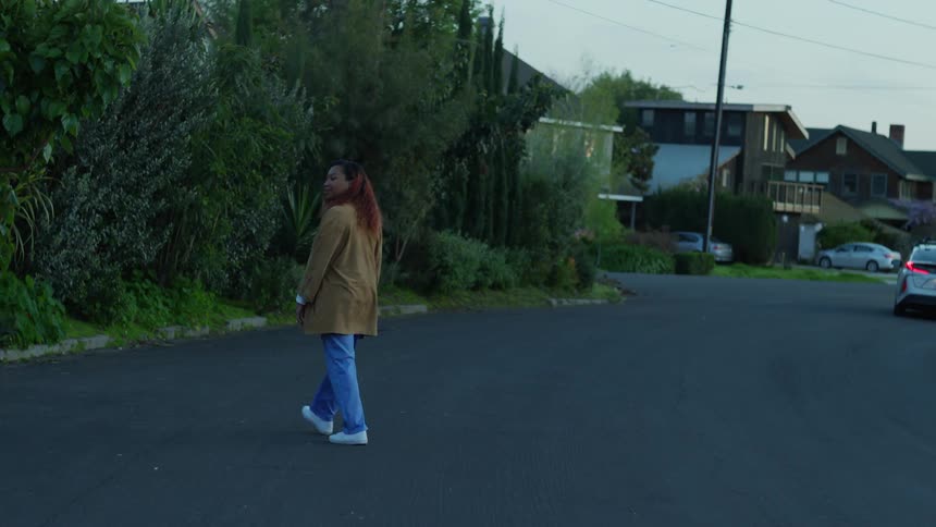 A woman wearing scrubs and a coat stands in the street as a car passes by
