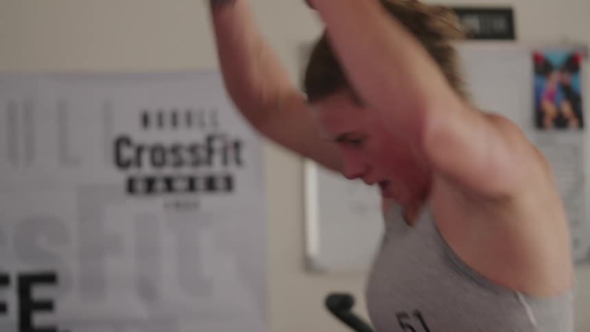 A muscular woman does weighlifting exercises at a gym using pulldown ropes