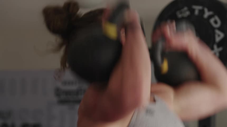 A woman is lifting kettle bells above her head