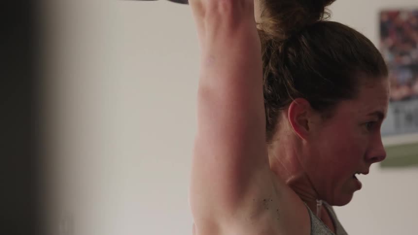 Close up of the face and arms of a strong muscular woman lifting weights over her head
