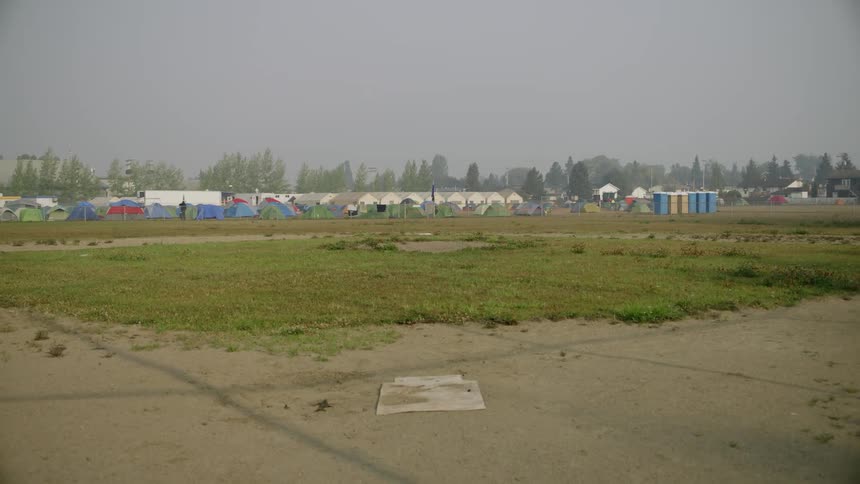 An old baseball field overgrown and tents set up in the distance beyond the field