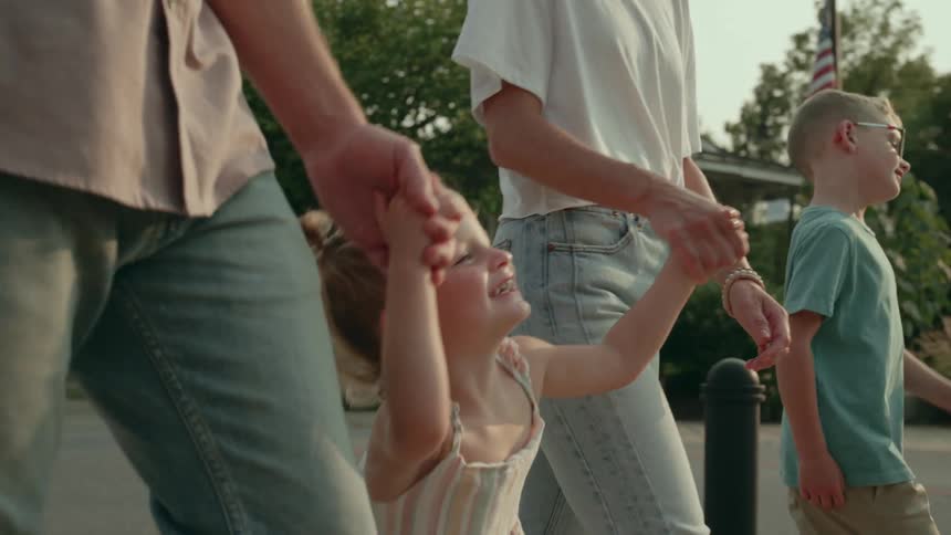 A young girl looks up at her parents while smiling as the family walks along a sidewalk