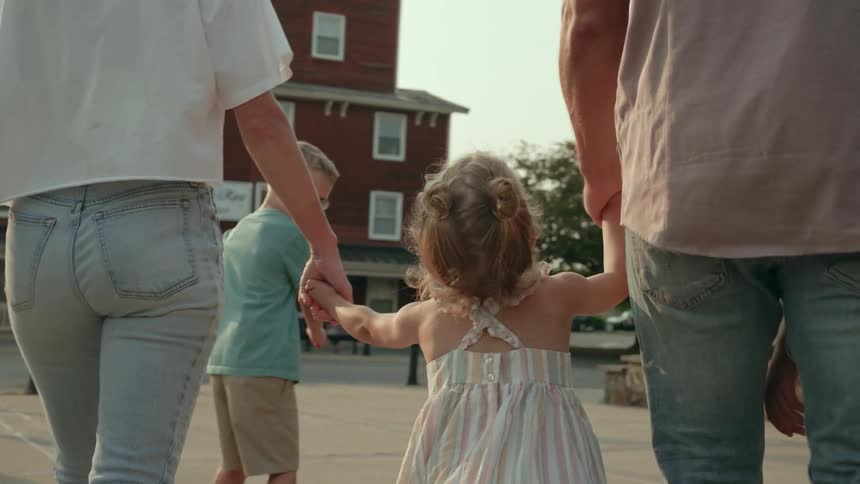 A father and mother hold their daughters hands while walking with their son toward a suburban street