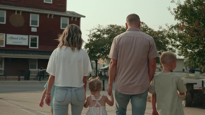 A family of a mother father two sons and a daughter walk through a suburban neighborhood toward a street