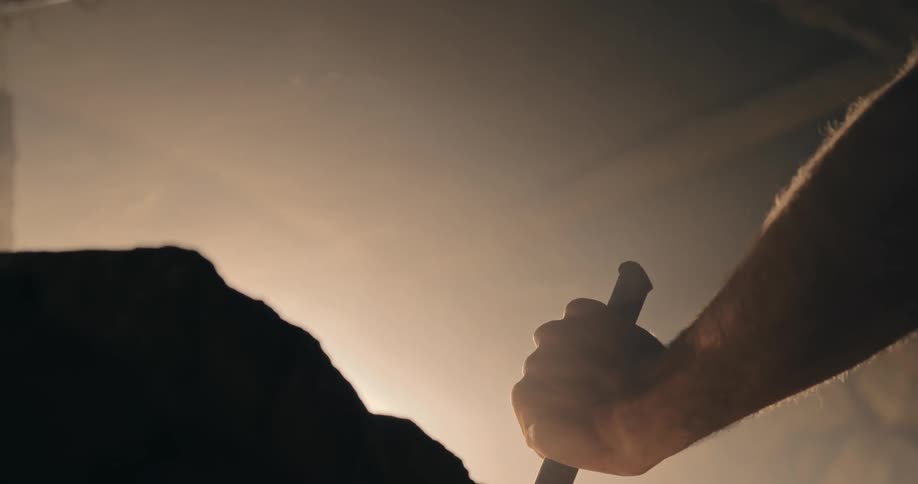 A man hammers a metal stake into a rock with a smoky haze around it