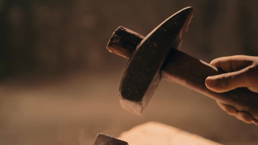 A close up of a person using a tool to hammer stone