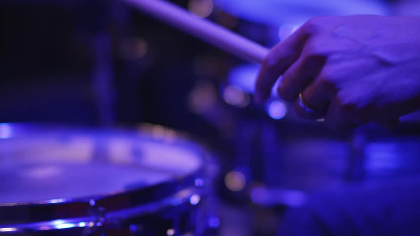 A man plays drums in a blue lit room