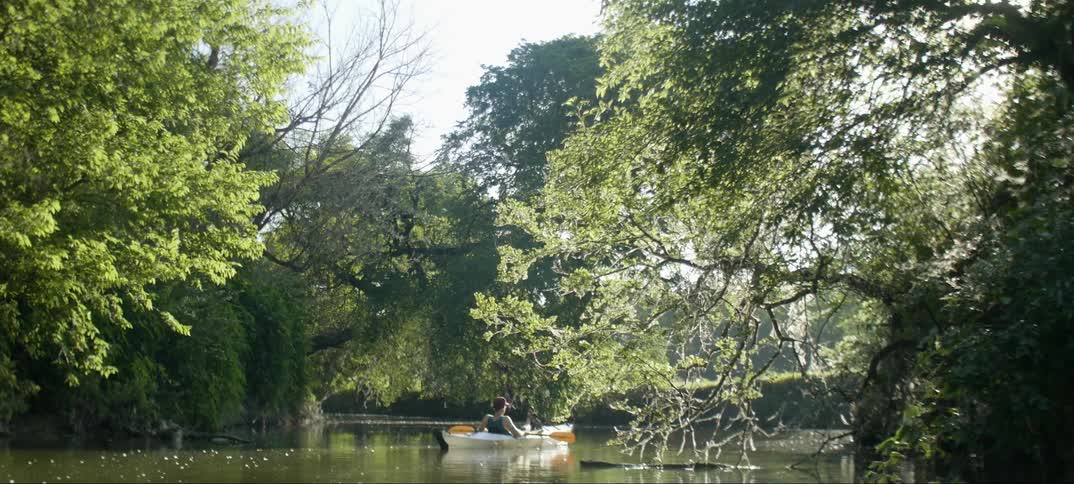 A person paddles a kayak down a stream