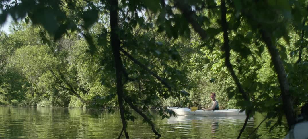 A man is riding his canoe in a small creek