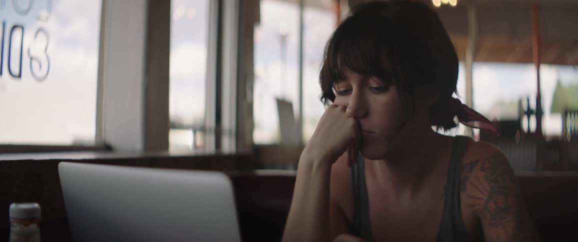 A woman sits at a table in a restaurant working on her laptop