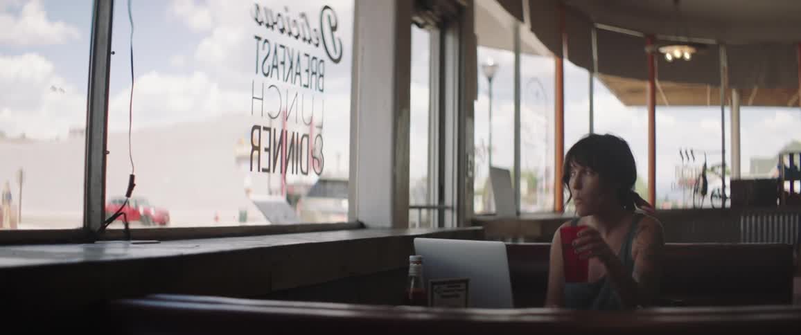 A woman takes a drink while sitting in a diner with a laptop