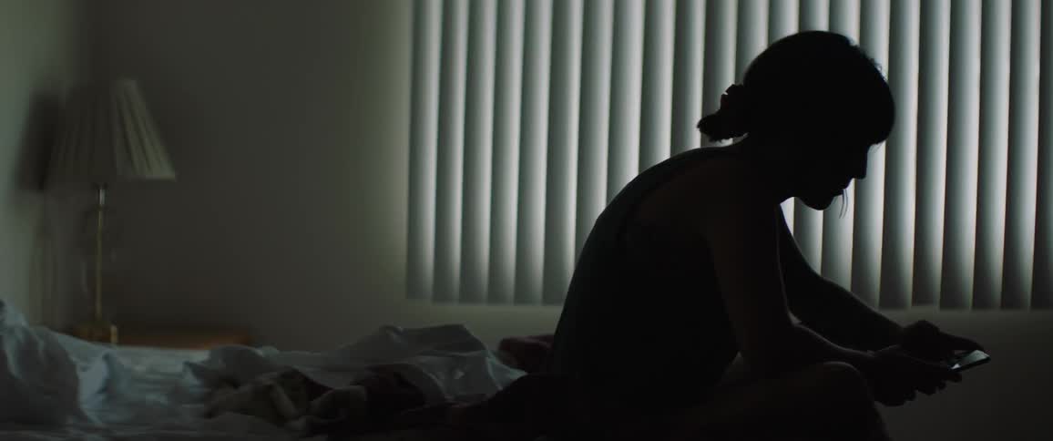 Woman sitting on the bed uses smartphone indoors