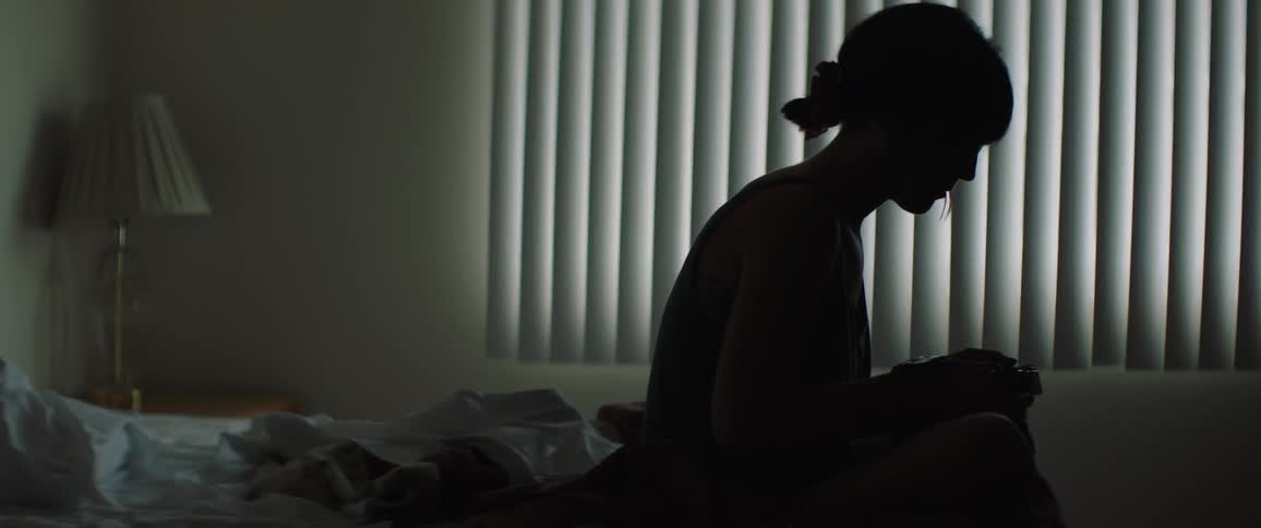 A girl sits in a dark room and looks in her camera