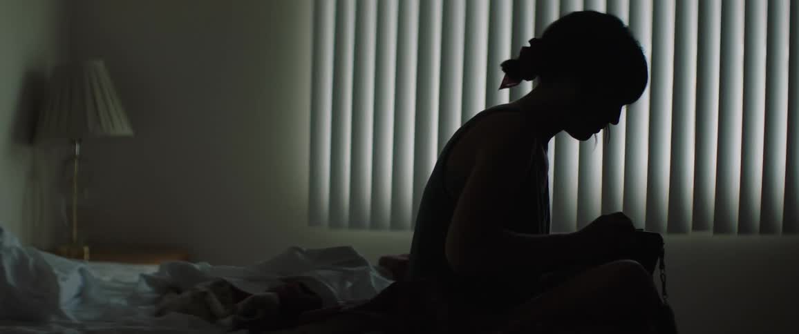 Woman sitting on the bed holds camera in the dim light in the bedroom