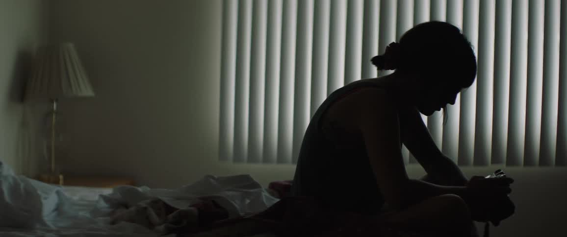 A woman sits on her bed and looks at photos on a digital camera