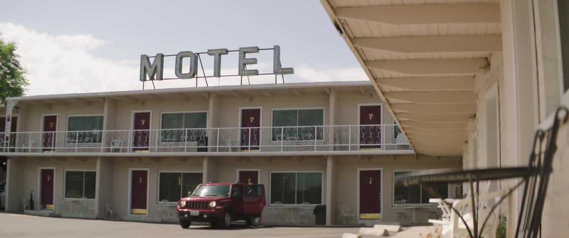 A girl outside of a motel puts a backpack in her vehicle