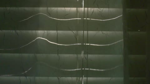 A curtain moves against closed blinds