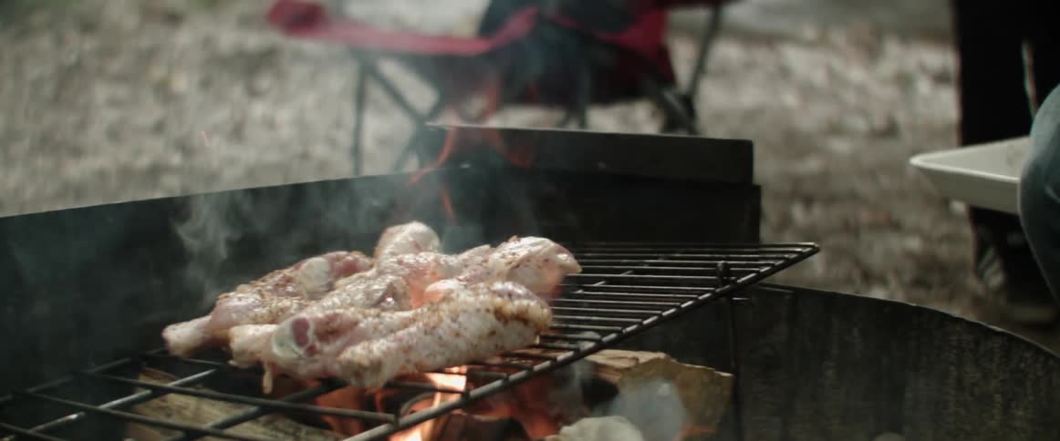A person cooking chicken legs on an outdoor campfire