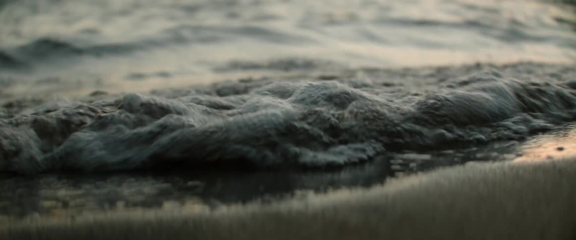 Waves breaking on a beach with pink reflecting on the water