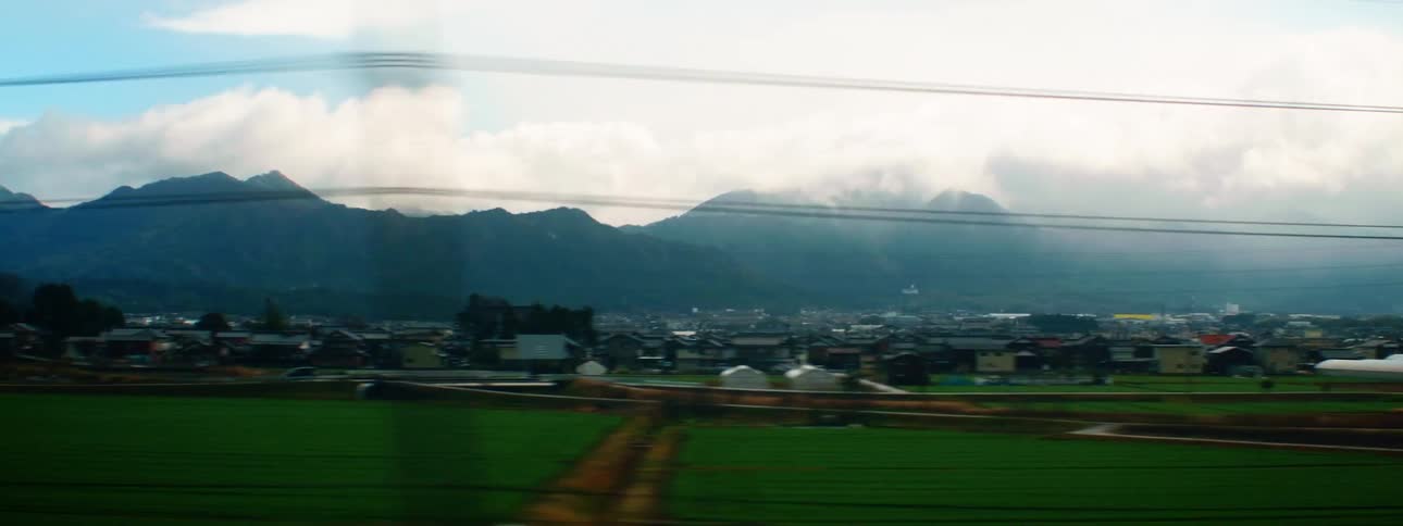 A grassy field with buildings a mountain range the sky and clouds in the background