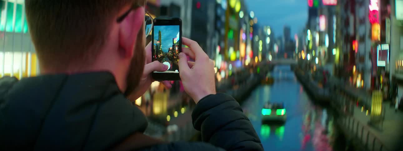 A man in a city takes a video of a boat in a canal with his cell phone