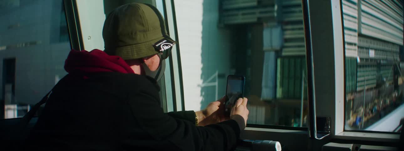 A man on a subway going through the city sits and looks at his cell phone