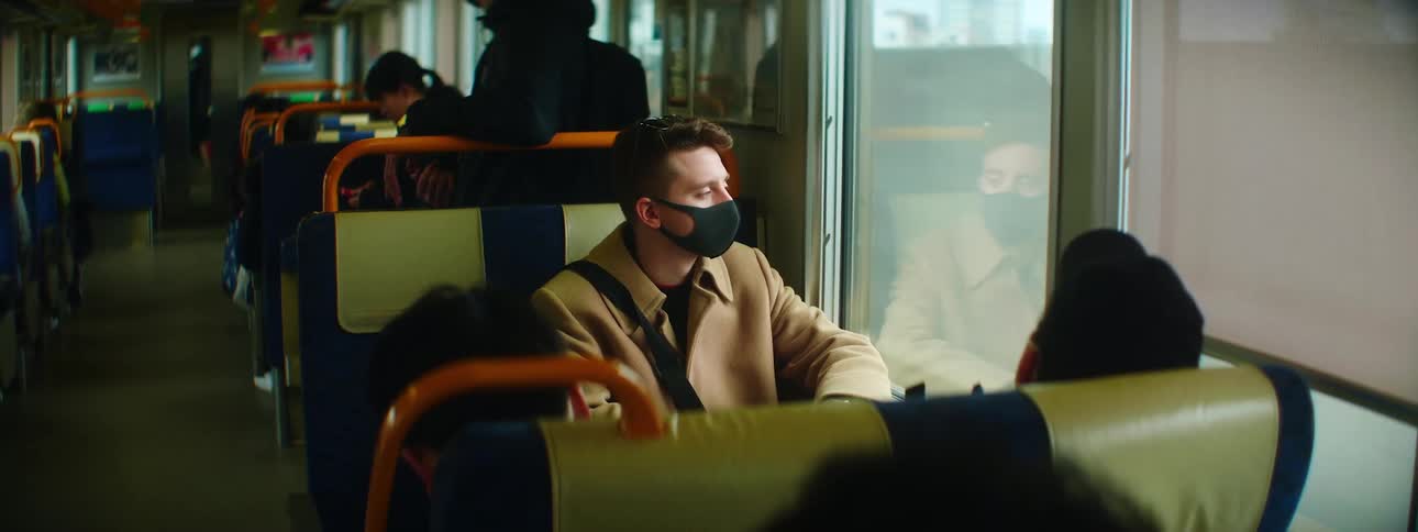 Man wearing mask looking out window of moving train car