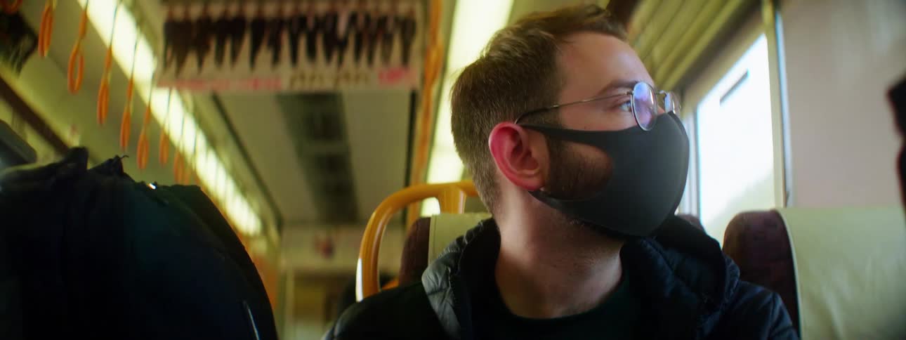 A man with a mask and glasses sitting on a train