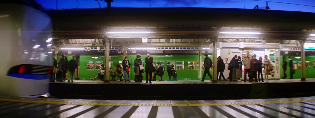 A train station with people standing with a train departing and the sky in the background