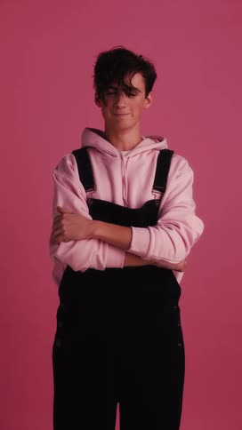 A white teenager stands with his arms crossed while wearing overalls