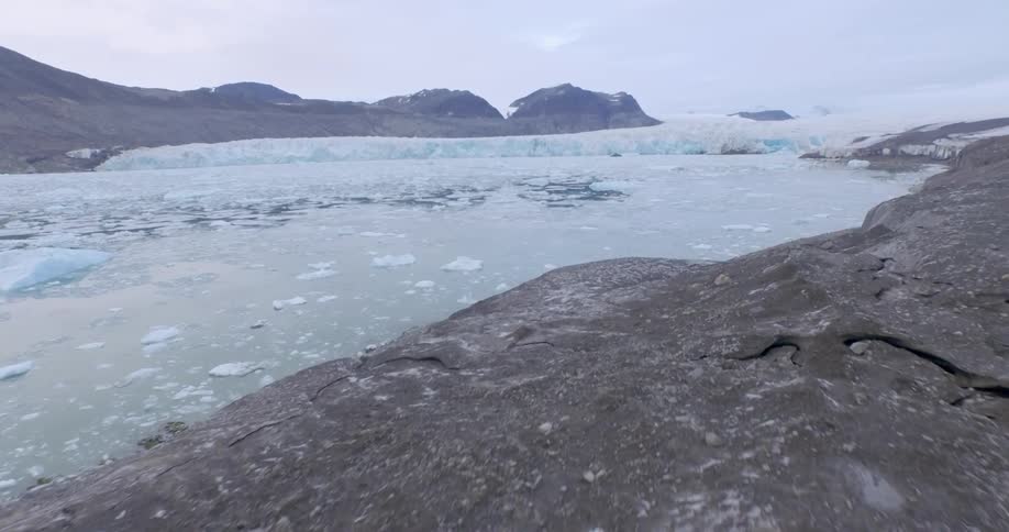 A group of people are standing looking out across the water toward a glacier