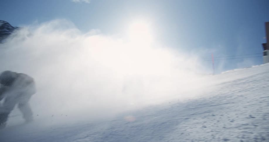 A snowboarder descends a snowy piste on a clear day