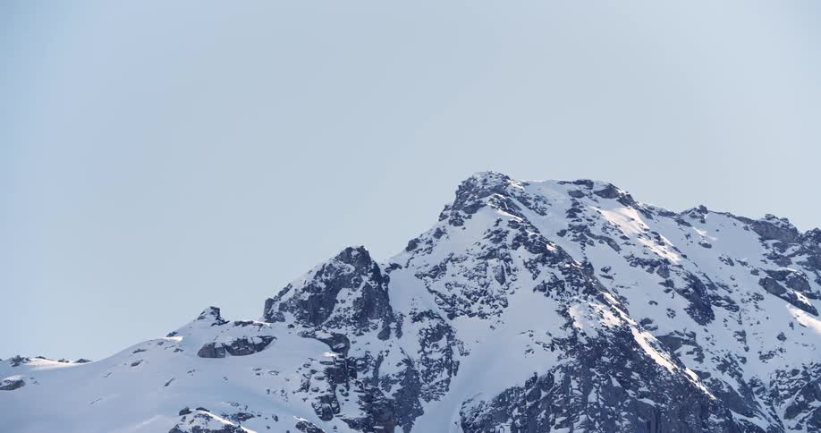 The sun shines on a snow covered mountain with a peak high in the sky
