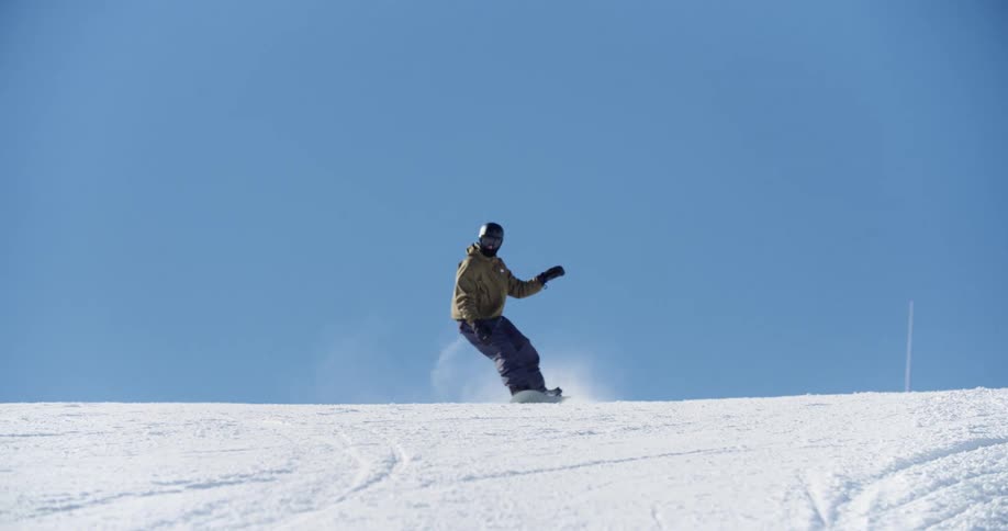 A snowboarder weaves left and right as he comes over the hill toward the camera