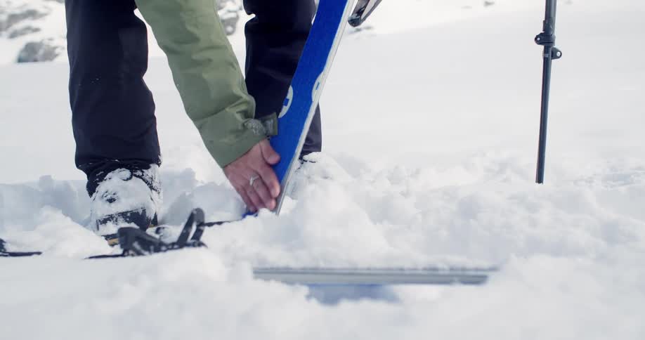 Person standing in snow with ski gear pressing down ski binding skins in preparation