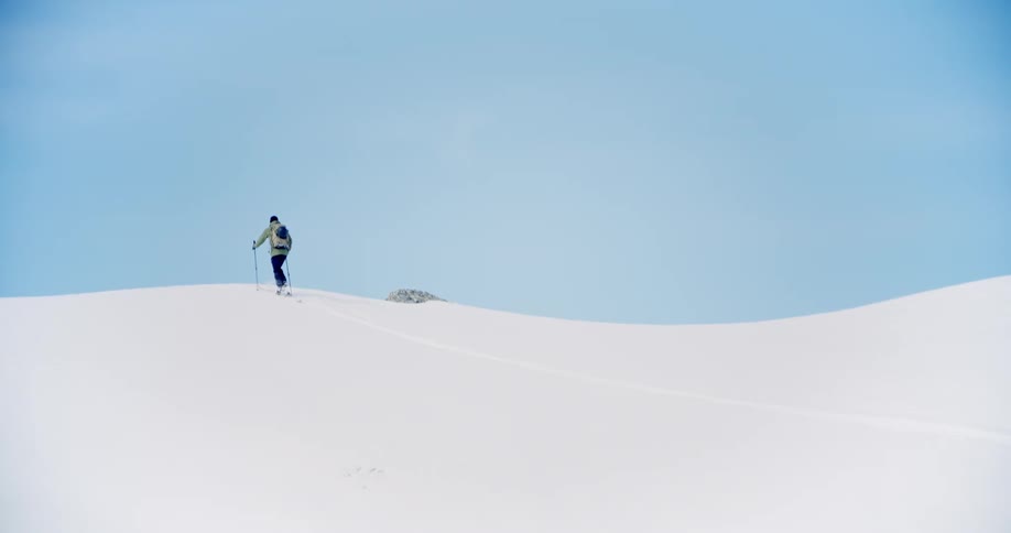 Man in the distance cross country hiking or skiing up snowcovered hill